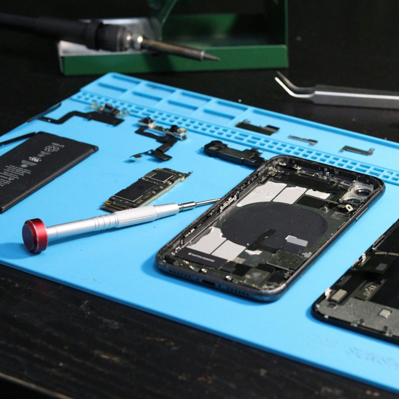 Close-up of disassembled smartphone parts on a blue repair mat with tools.